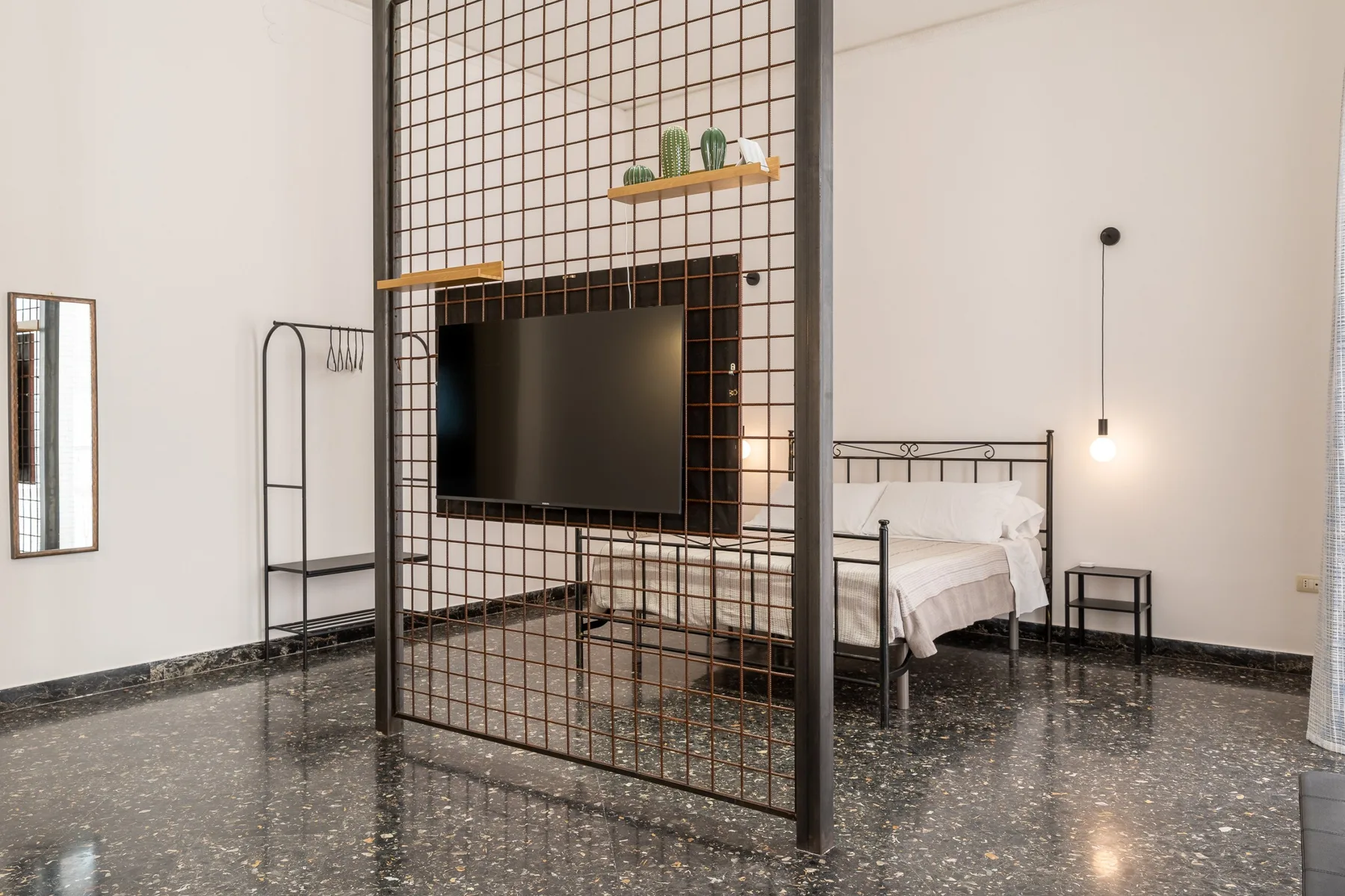 Un dormitorio con una cama, un televisor y un separador metálico abierto.