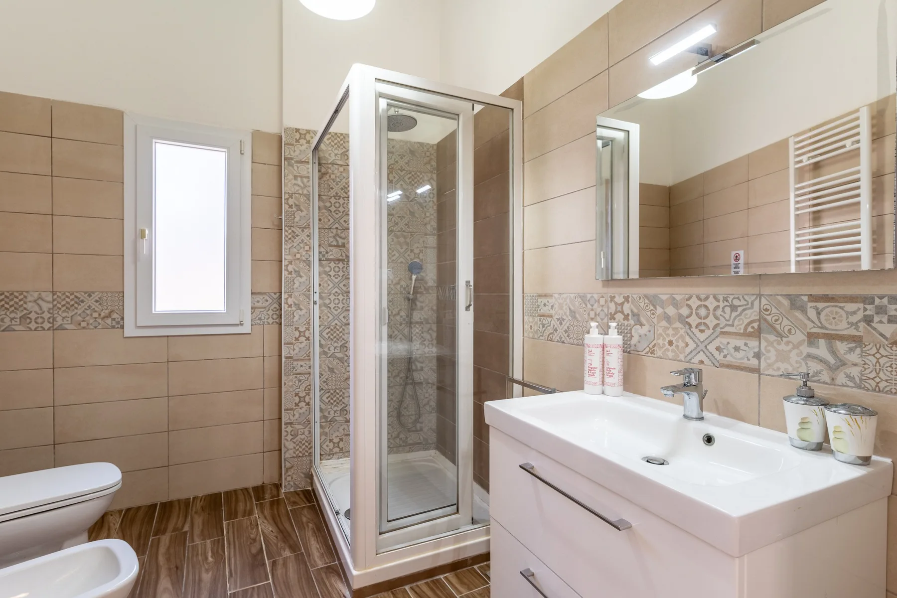 Un baño alicatado con ducha de vidrio, lavabo y espejo de pared.