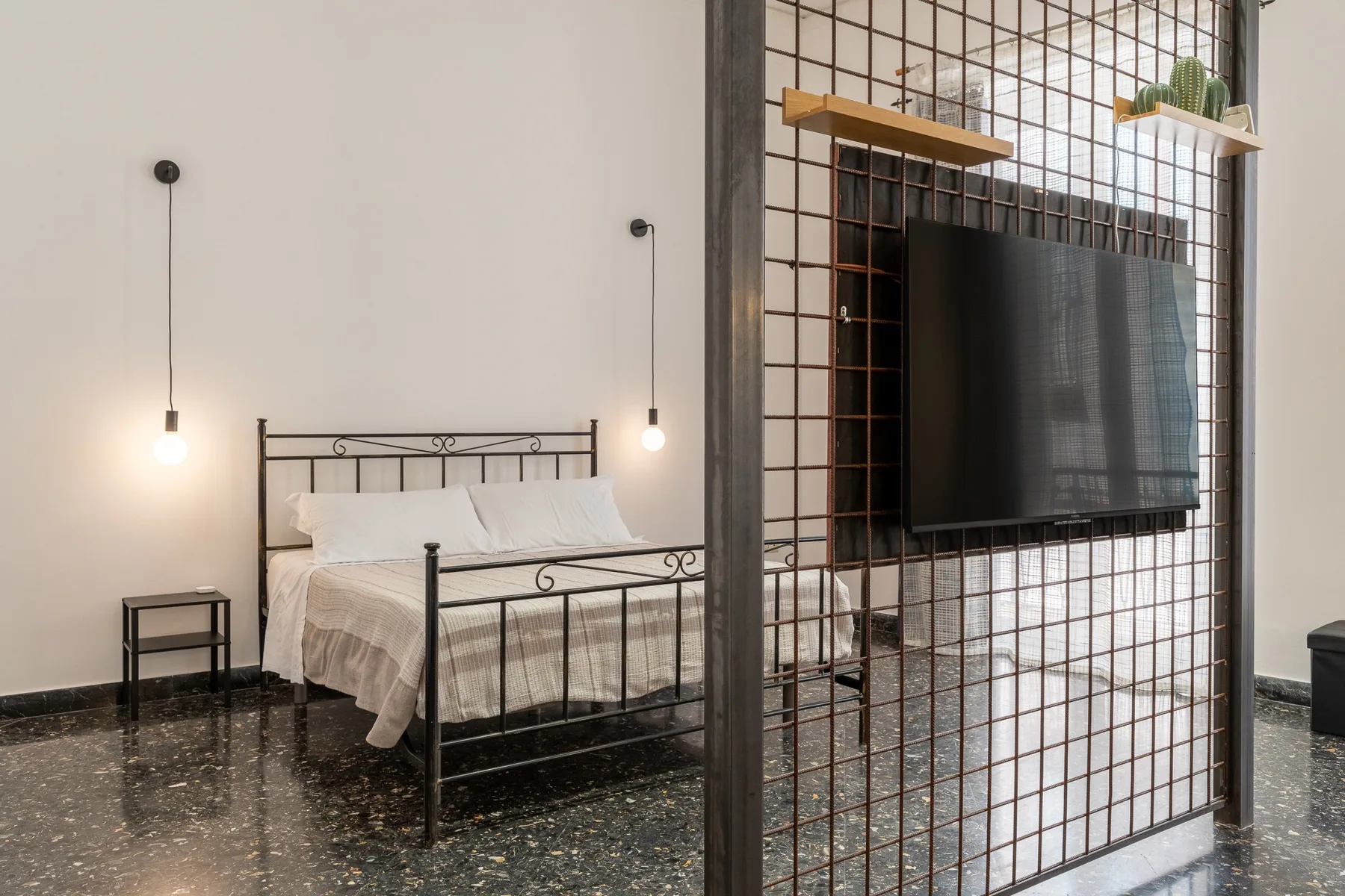 Un dormitorio con una cama de metal y un televisor montado en una división de rejilla.
