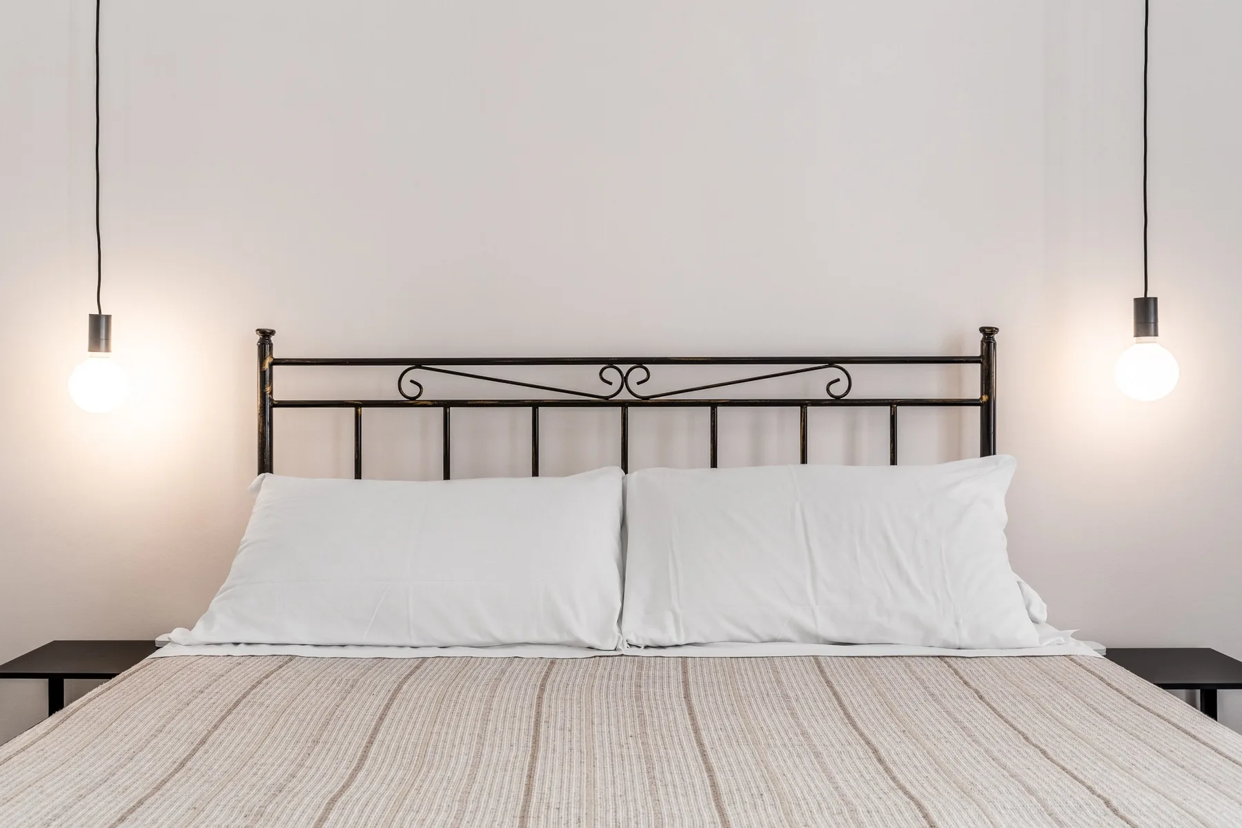 Un dormitorio con una cama bien tendida y dos lámparas colgantes.
