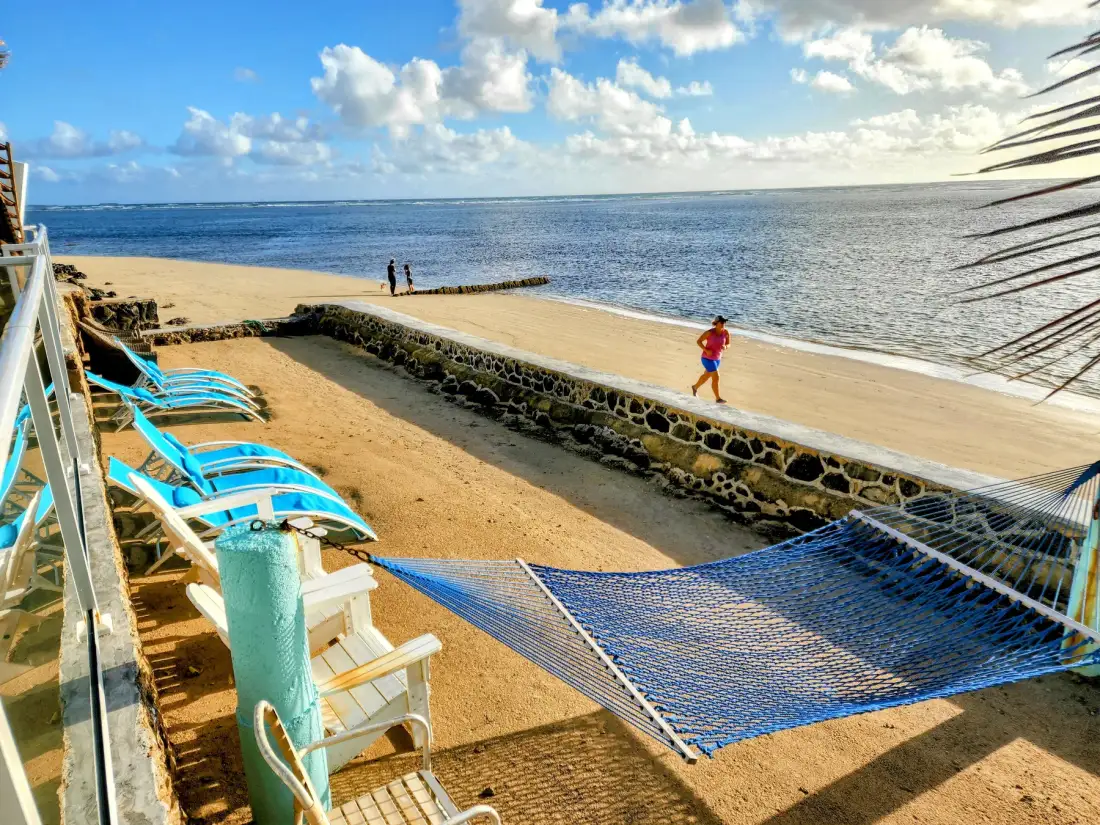 Una zona arenosa junto al mar, con asientos azules y una hamaca cerca del agua.