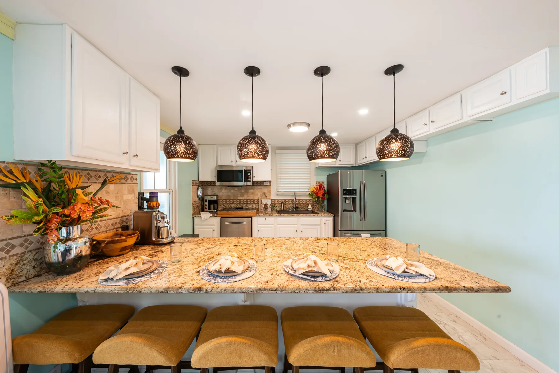 Una cocina luminosa con una barra larga y lámparas colgantes sobre los asientos.