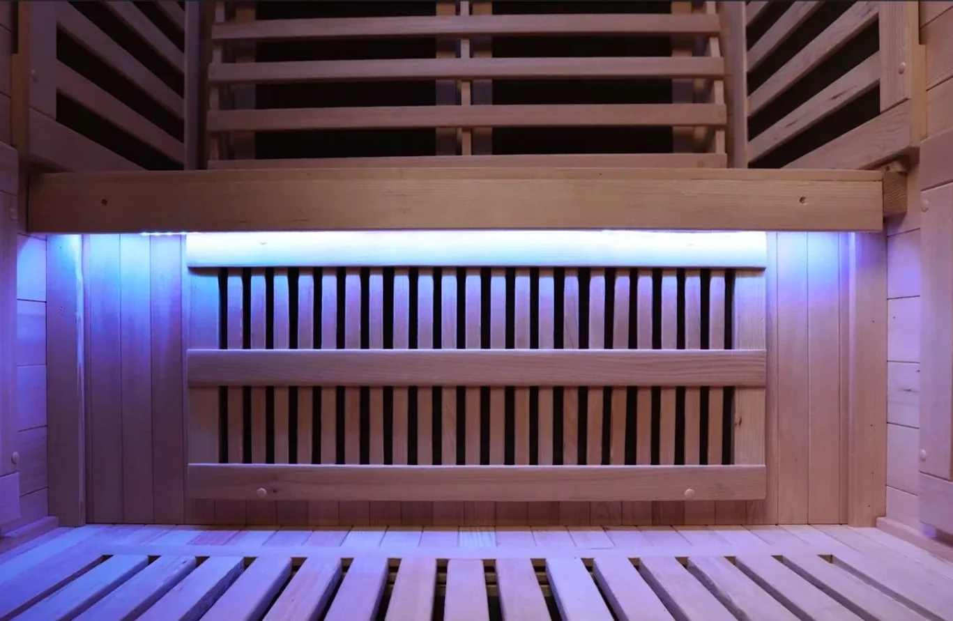 Interior de una sauna de madera con bancos de listones e iluminación azul.