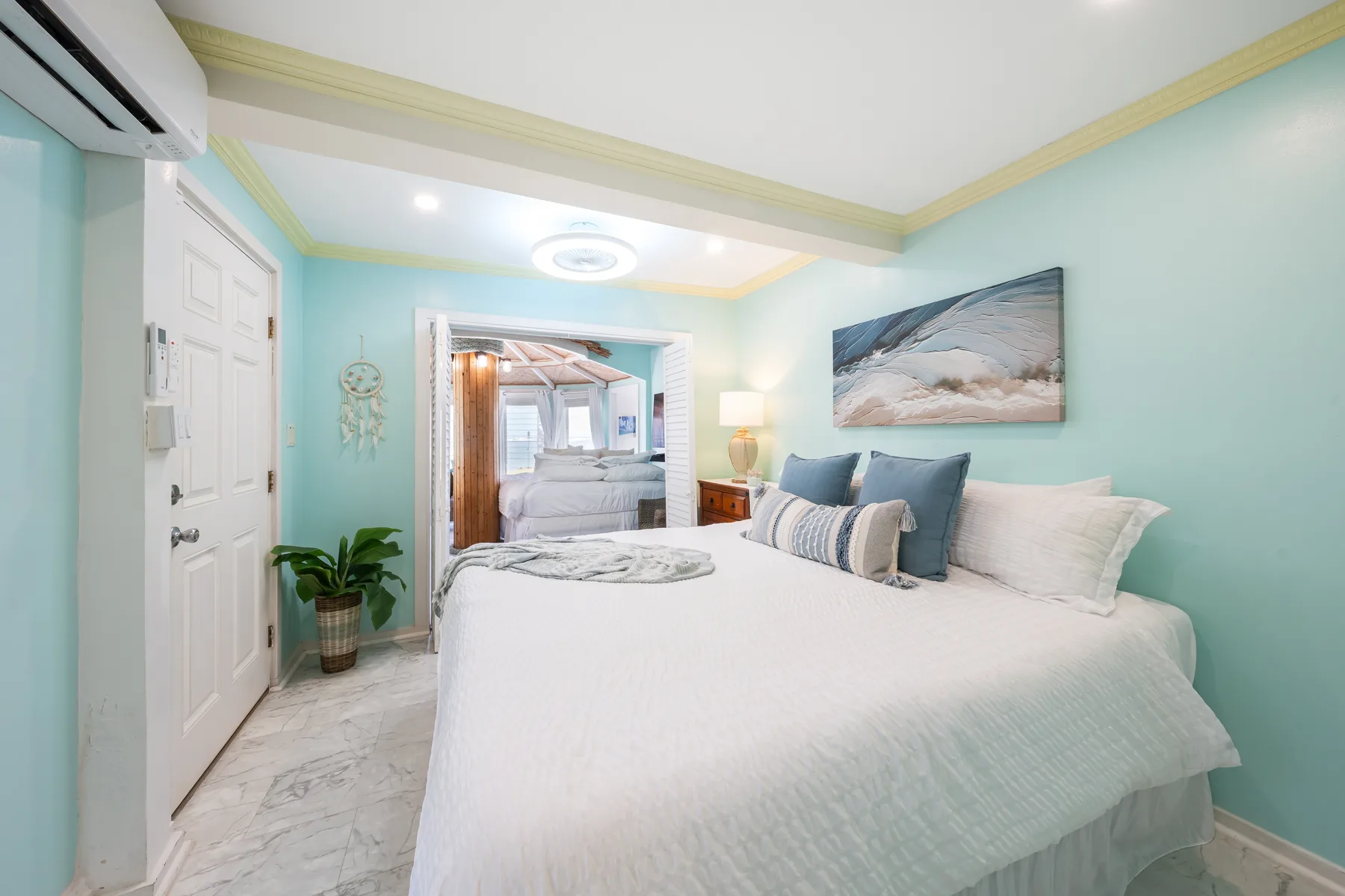 Un dormitorio luminoso con una cama grande, paredes azul claro y arte costero.