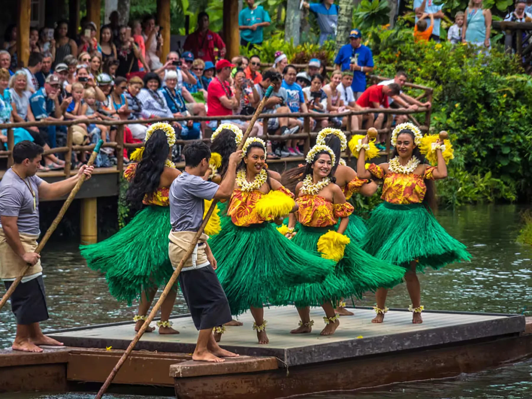 Artistas bailan con trajes coloridos en una plataforma flotante ante el público.