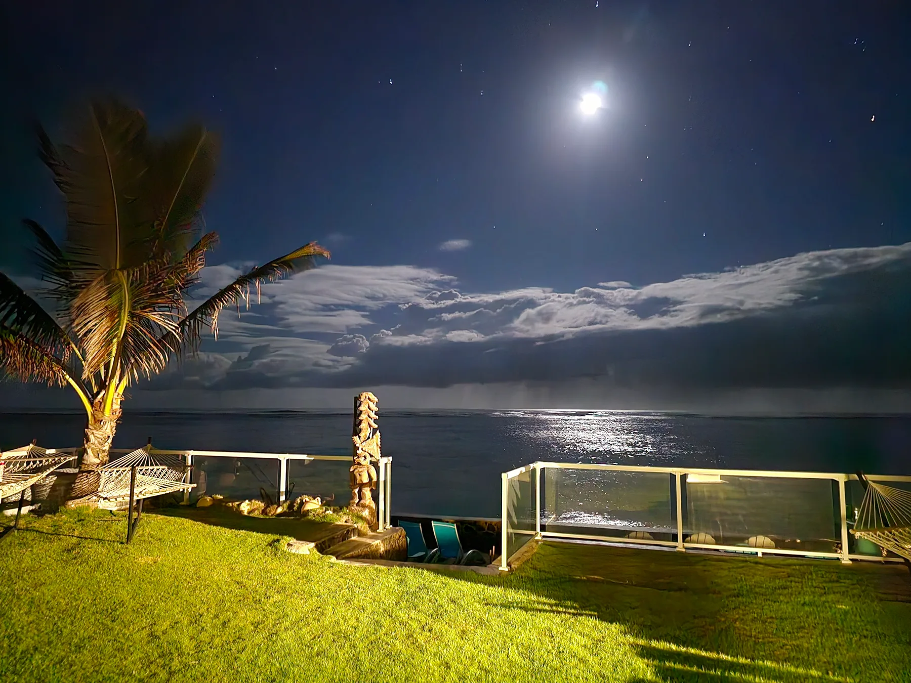 Un césped junto al agua, iluminado por la luna, mira hacia un cielo nocturno nublado.