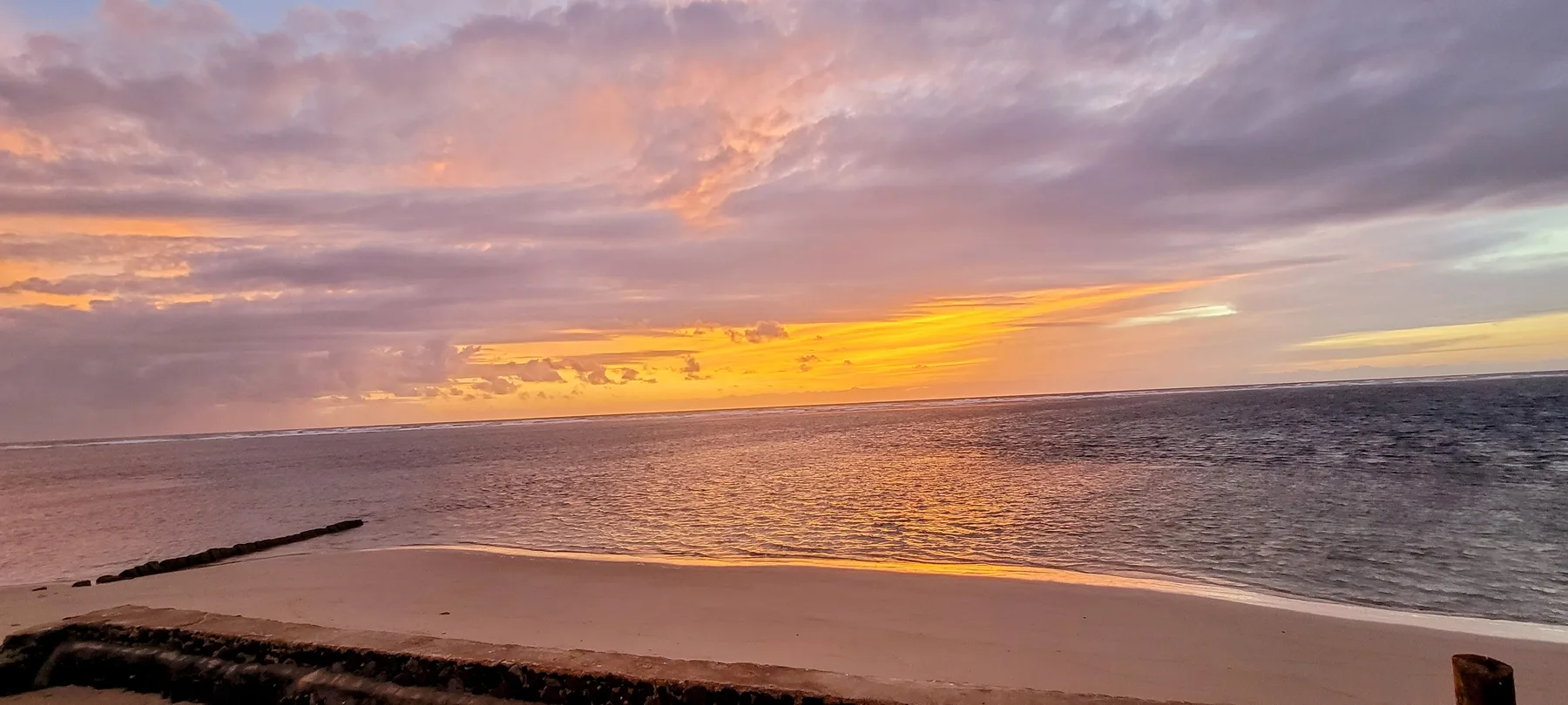 Una playa al atardecer con nubes de colores sobre el océano.