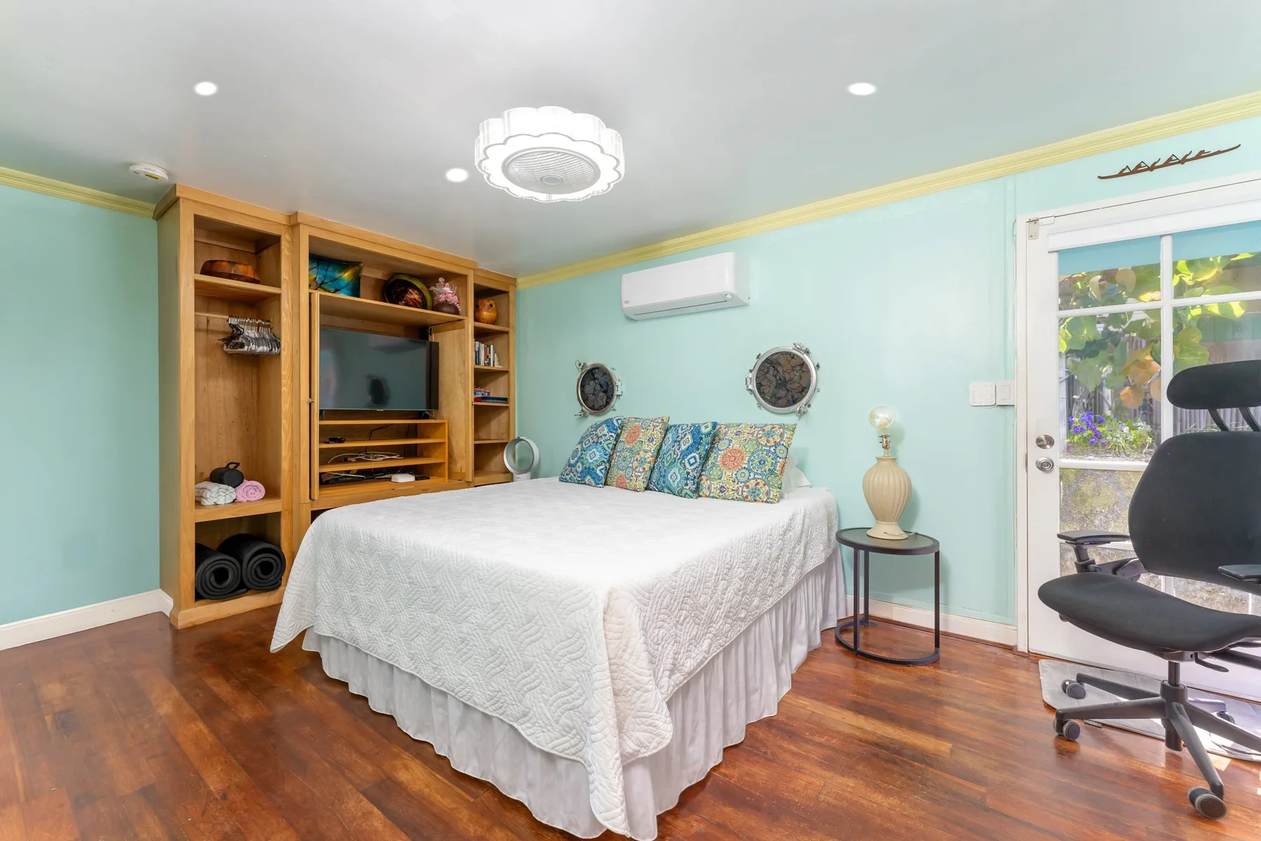 Un dormitorio con una cama, estanterías de madera y una silla de escritorio junto a una puerta de vidrio.