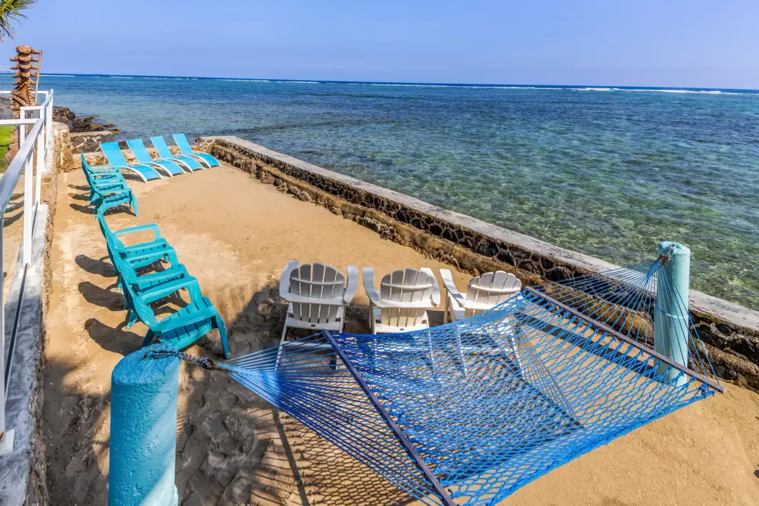 Una terraza junto al mar con asientos reclinables y una hamaca azul junto al agua.