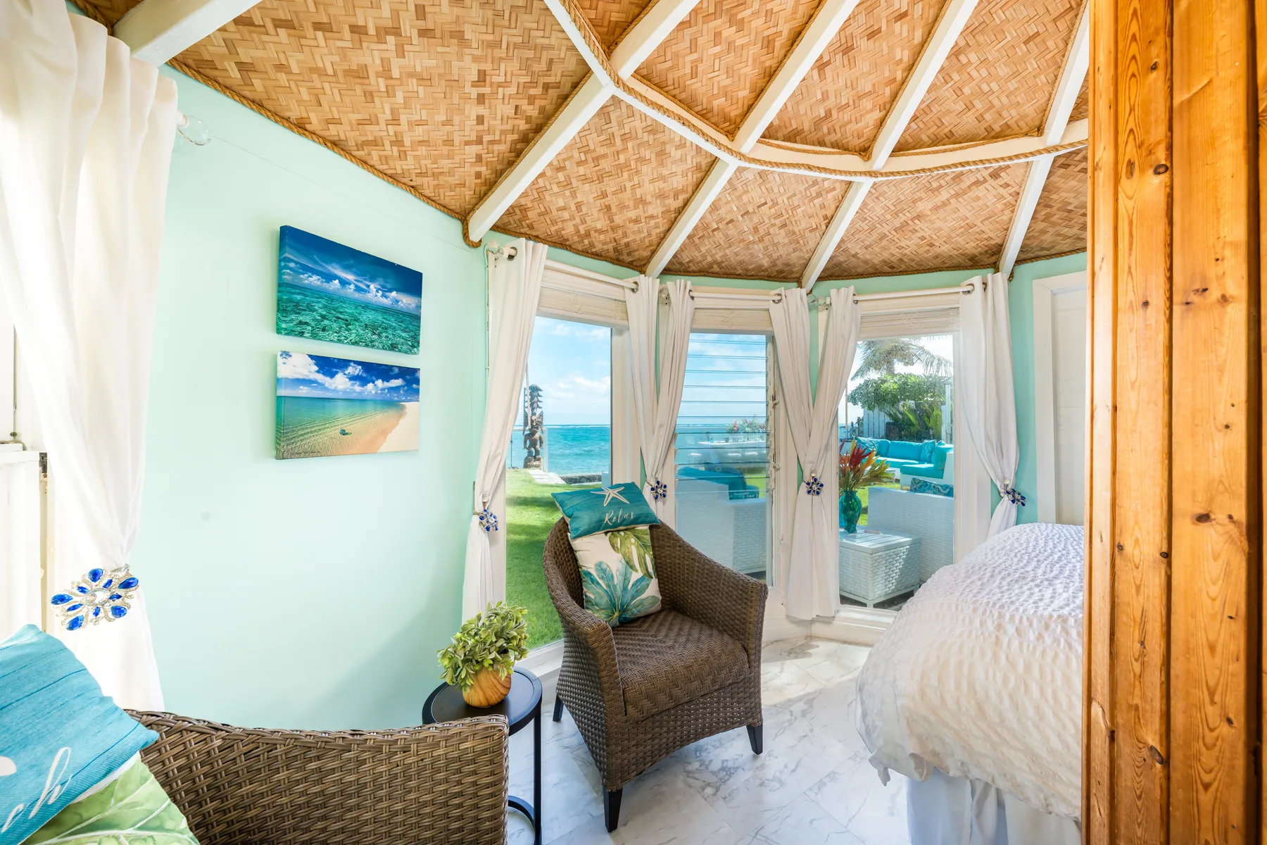 Un dormitorio luminoso con asientos de mimbre, una cama y ventanas con vistas al mar.