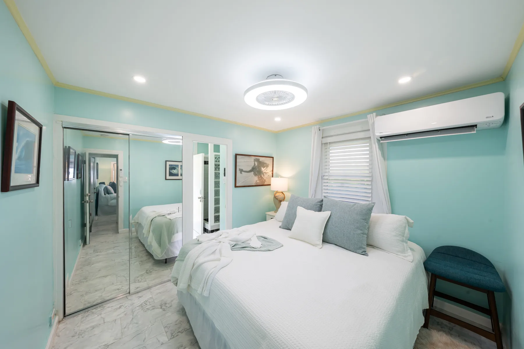 Un dormitorio con una cama bien tendida, un armario con espejo y una ventana.