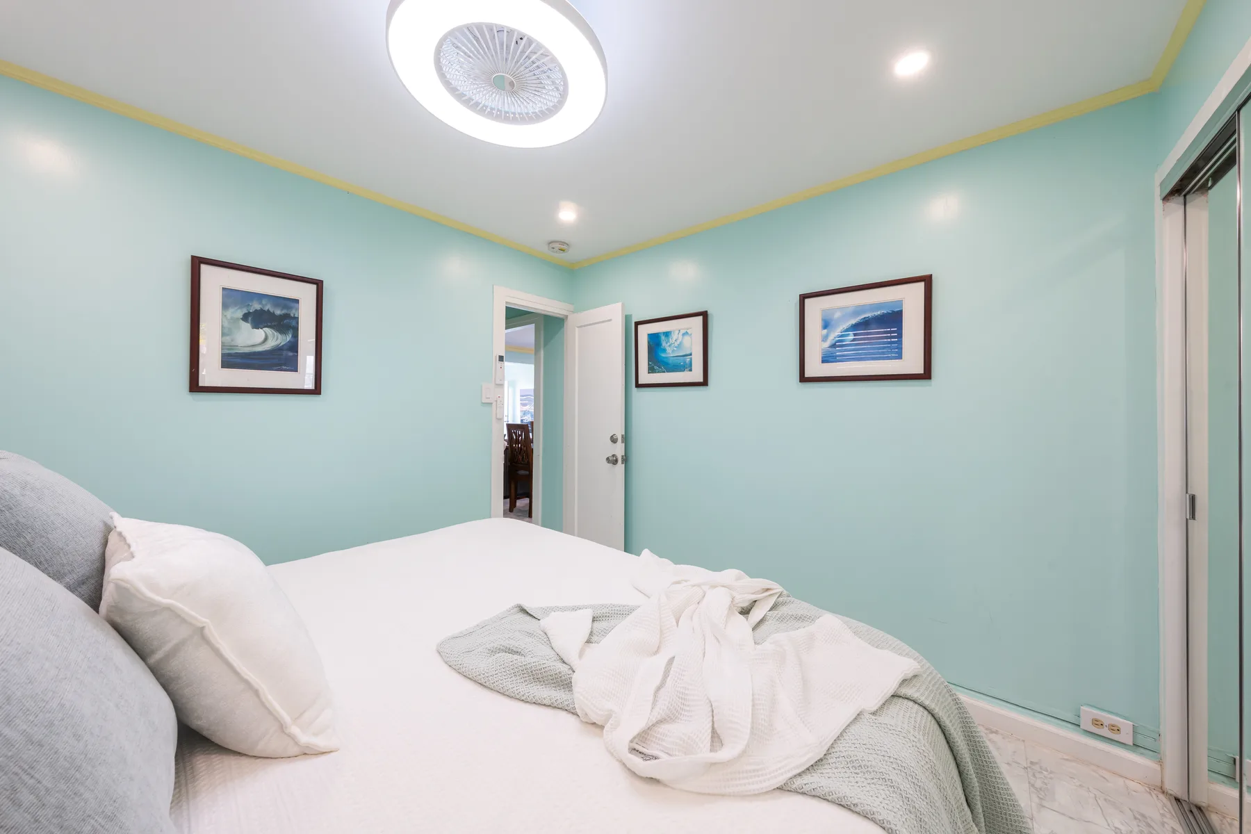Un dormitorio con una cama, paredes verde agua claro y cuadros enmarcados.