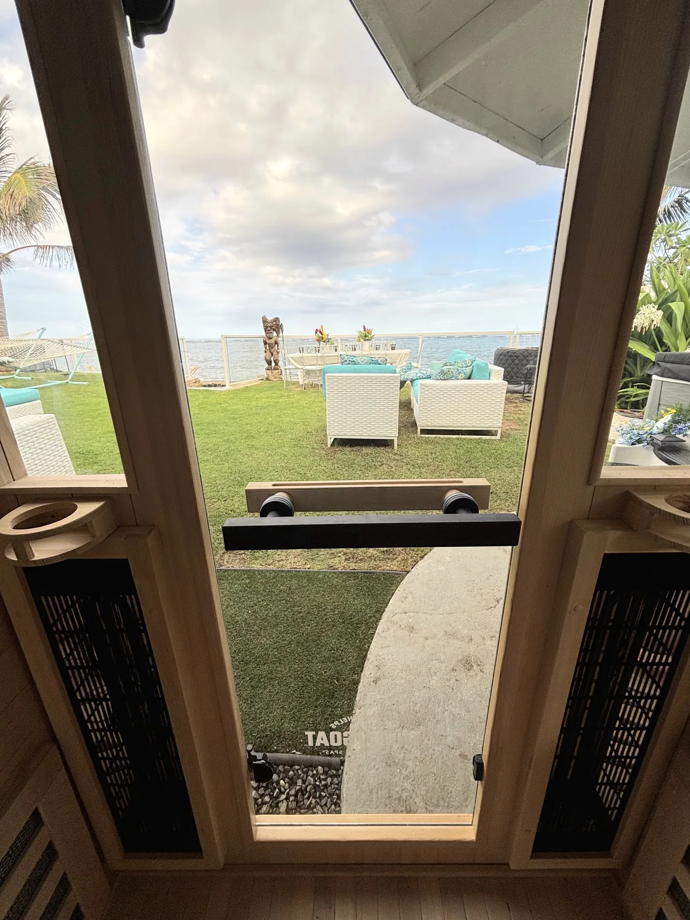 Una puerta de vidrio da a un patio junto al mar con césped y asientos al aire libre.