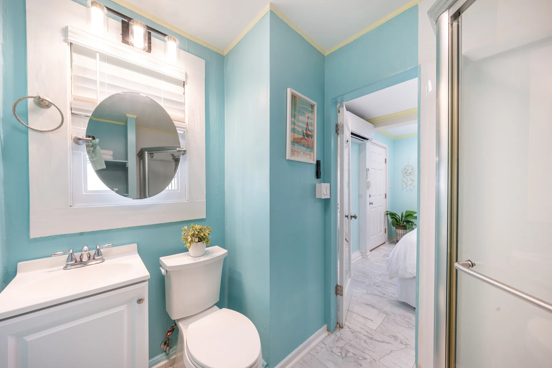 Un baño turquesa tiene un lavabo, un inodoro y un espejo redondo.