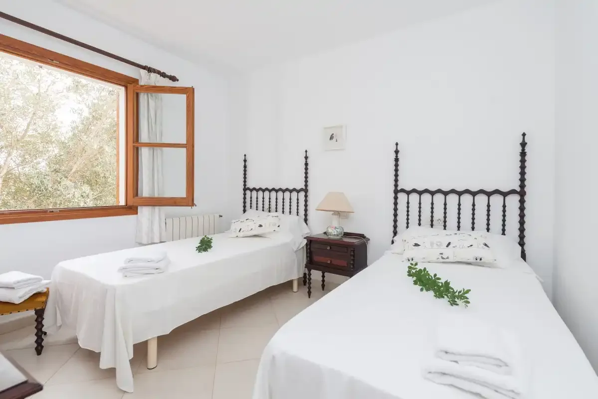 A bright bedroom with two single beds beside a large wooden-framed window.