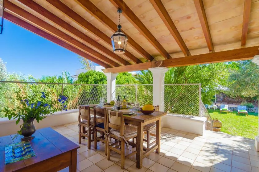 A covered outdoor dining area with a wooden table and garden views.