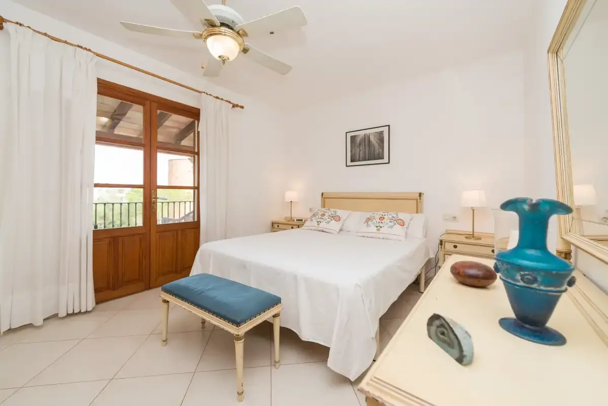 A bedroom with a bed, bedside tables, and a door opening onto a balcony.
