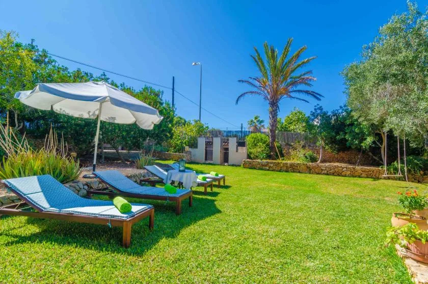 A sunny garden with a lawn, loungers, and a large patio umbrella.