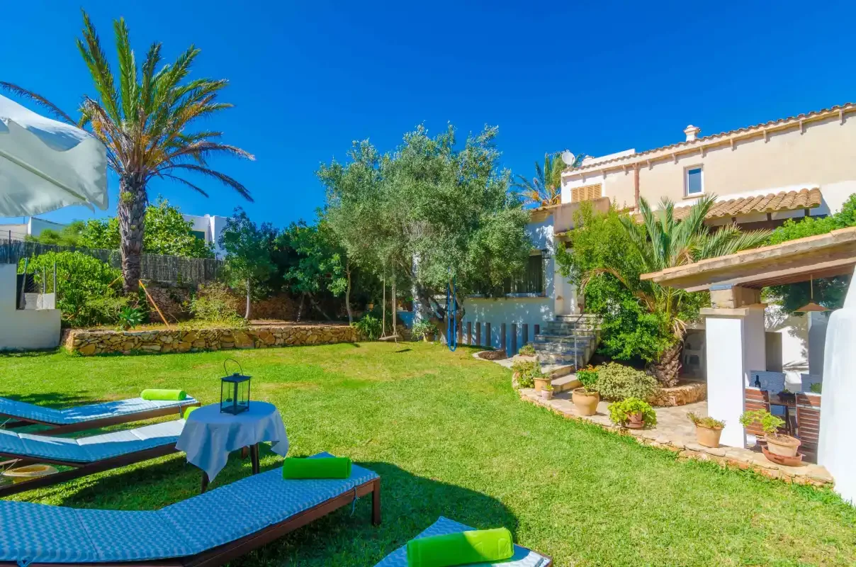 A garden courtyard with a lawn, outdoor seating, and a palm tree beside a house.