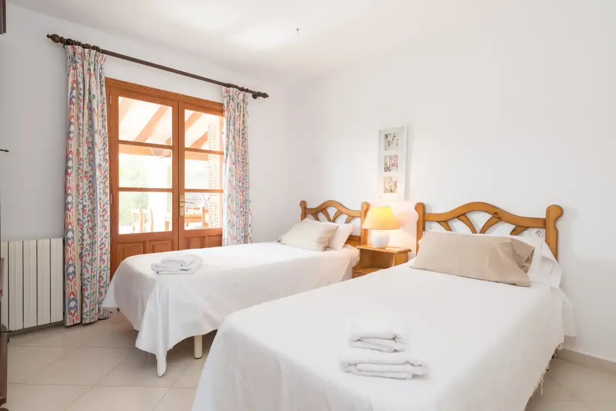 A bright bedroom with two beds, patterned curtains, and a wooden-framed window.