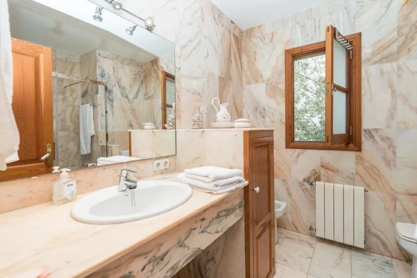 A marble-tiled bathroom with a sink, mirror, and open window.