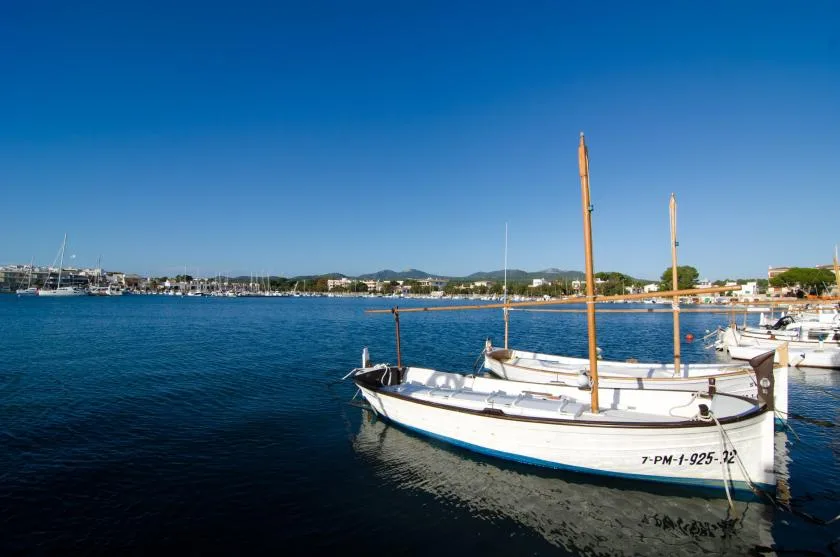 A small sailboat is moored in calm blue water near a distant shoreline.