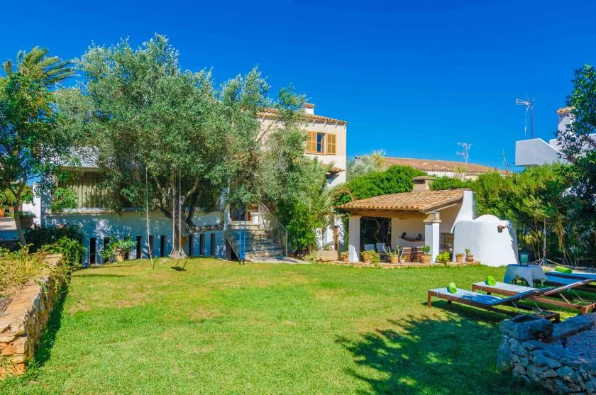 A sunny garden lawn in front of a house, with trees and loungers.