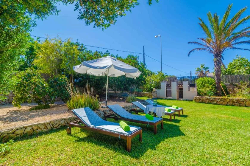 A sunny garden with outdoor loungers beneath a large shade umbrella.