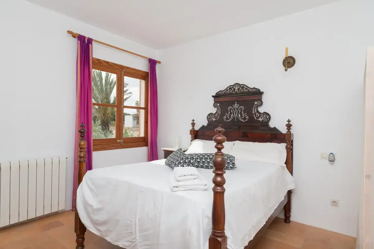 A bedroom with a carved wooden bed and a window framed by purple curtains.