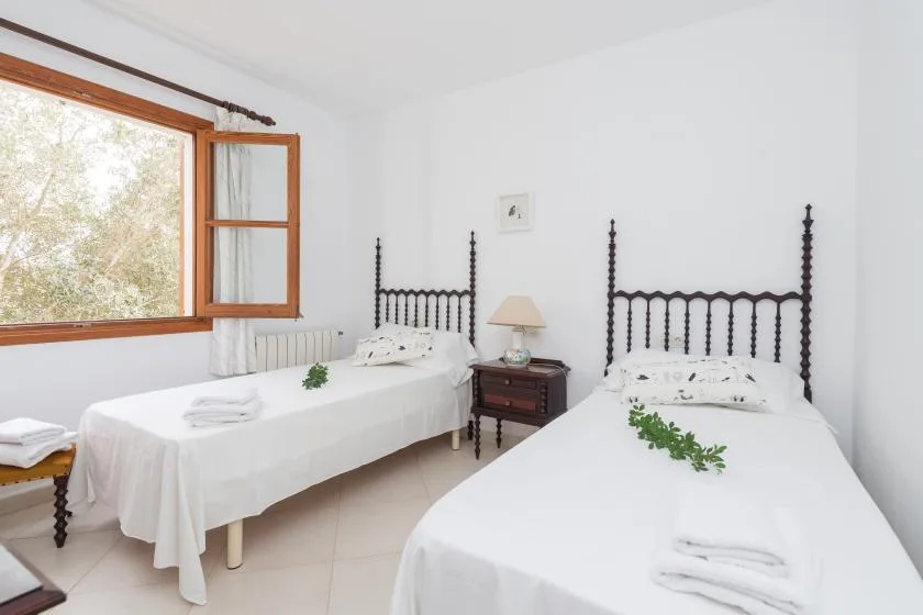 A bright bedroom with two beds beside an open window.