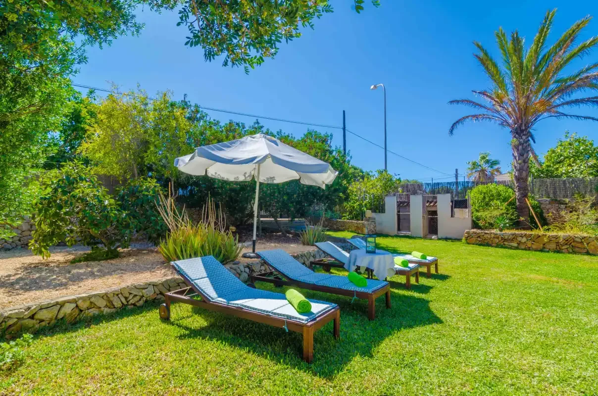 A sunny garden with loungers beneath a large shade umbrella.