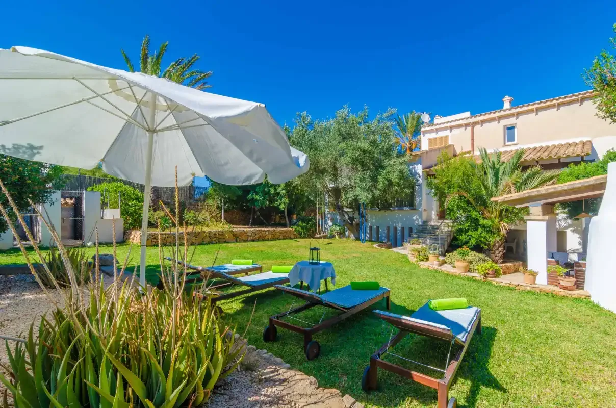 A sunny garden patio with lounge seating, an umbrella, and a house in the background.