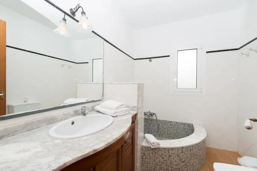 A bathroom with a long vanity, a mirror, and a tiled soaking tub.