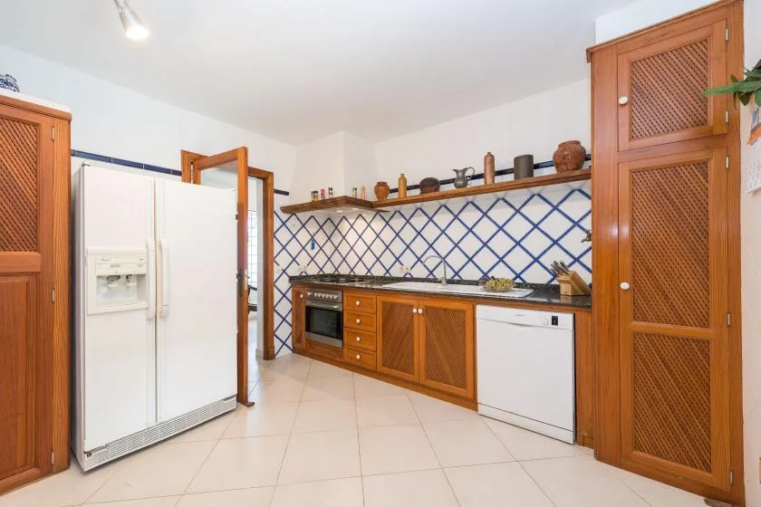 A bright kitchen with wooden cabinets, a refrigerator, and a blue diamond-pattern backsplash.