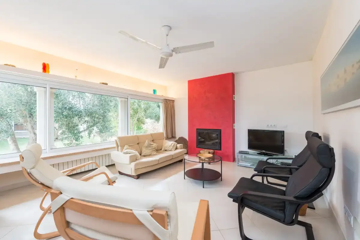 A bright living room with large windows, seating, and a television.