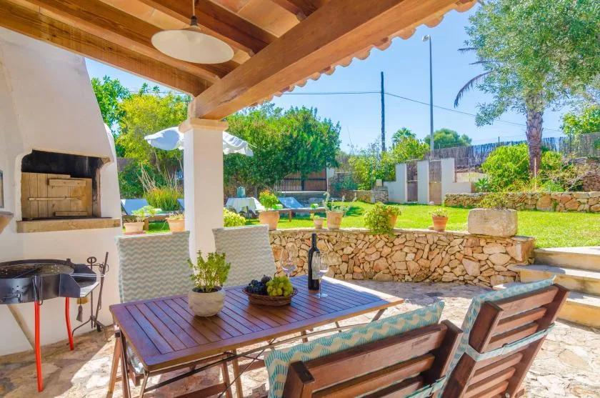 A covered outdoor dining area overlooks a garden, with a built-in grill nearby.