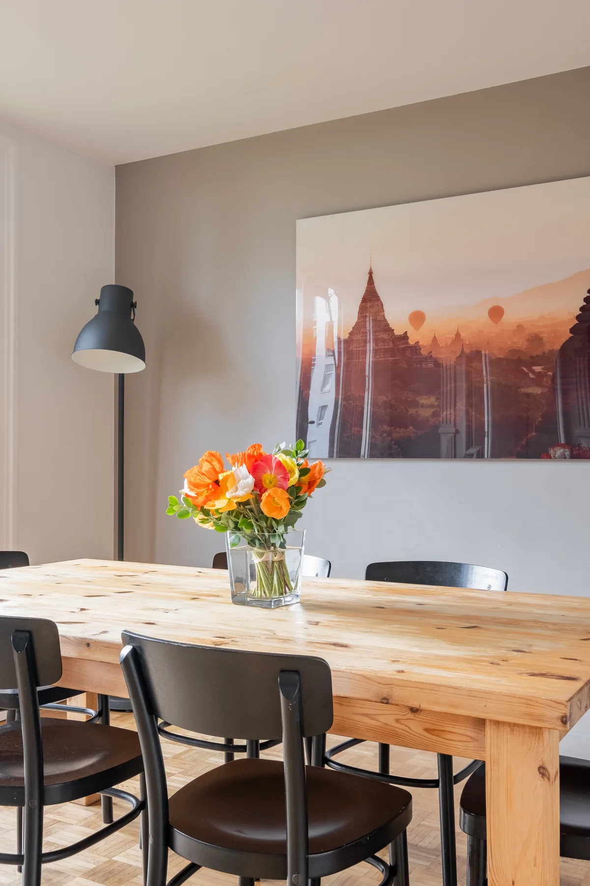 Un comedor con una mesa de madera, asientos oscuros y un colorido arreglo floral.