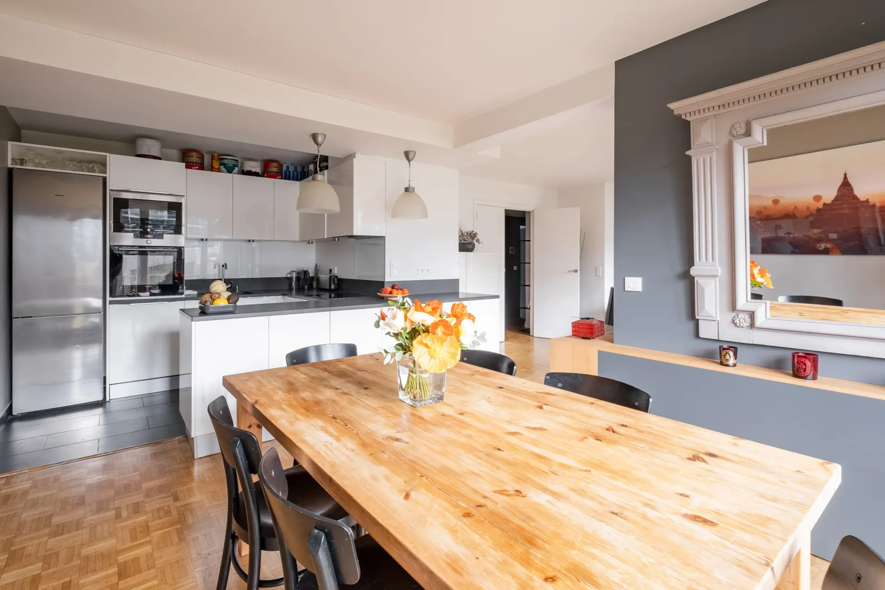 Una cocina luminosa con comedor, una mesa larga de madera y gabinetes blancos.