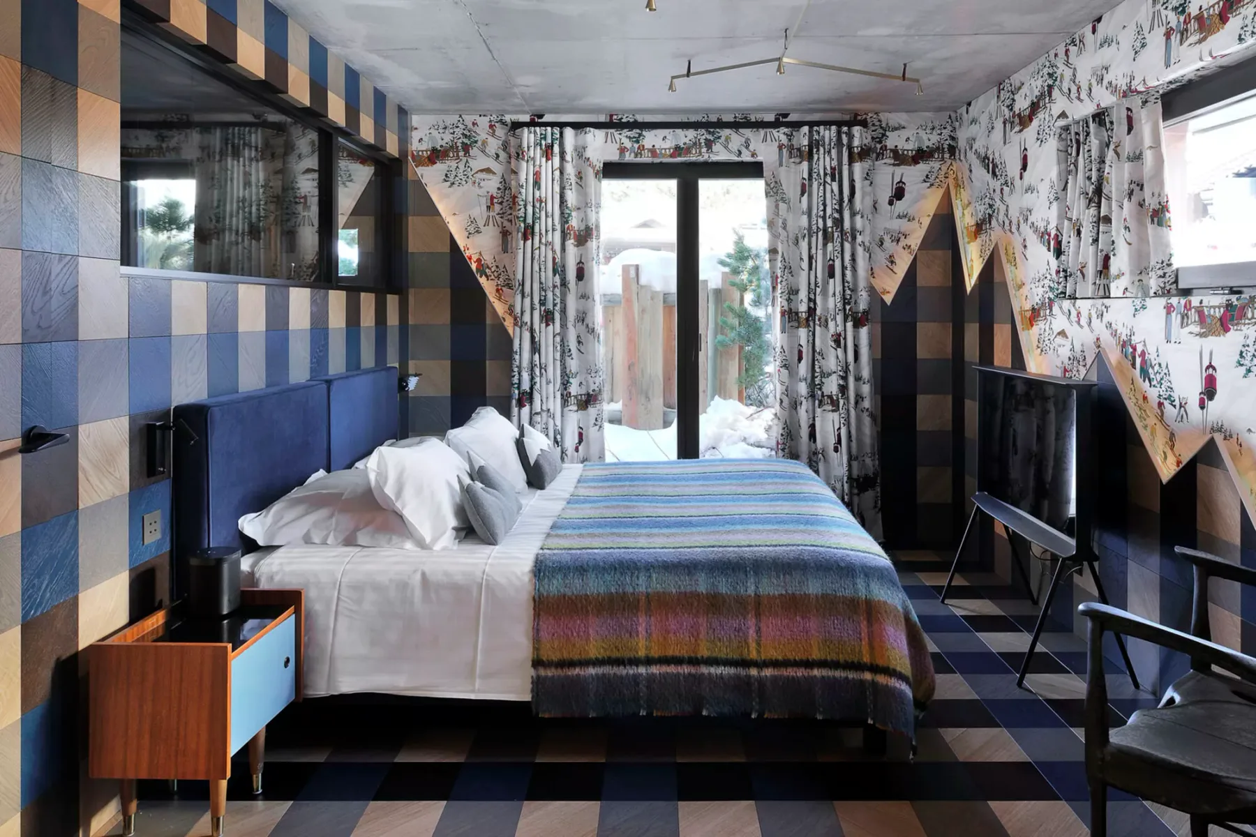 A bedroom with a bed covered by a striped blanket and patterned curtains.