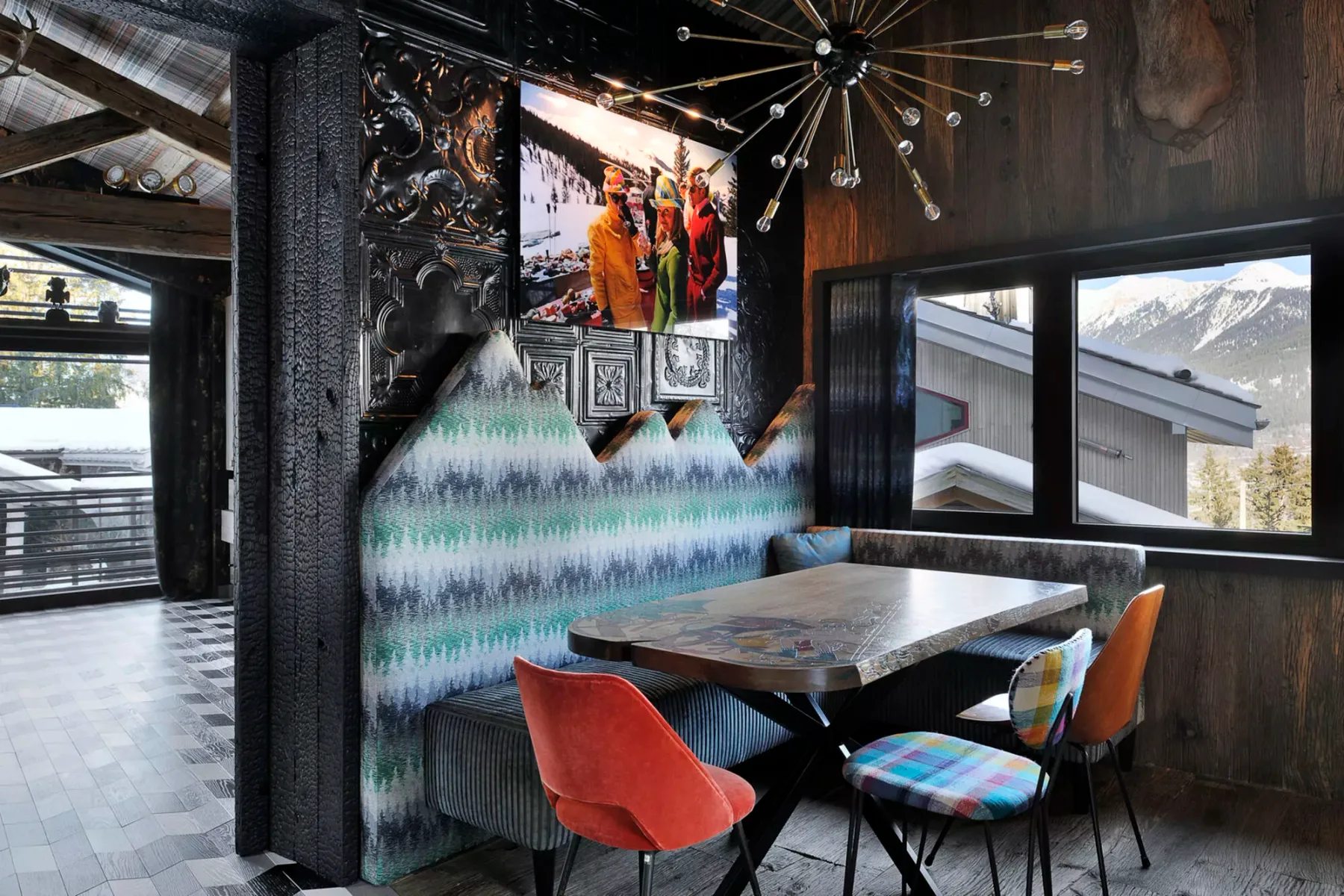 A dining area with a table, colorful seating, and large windows.