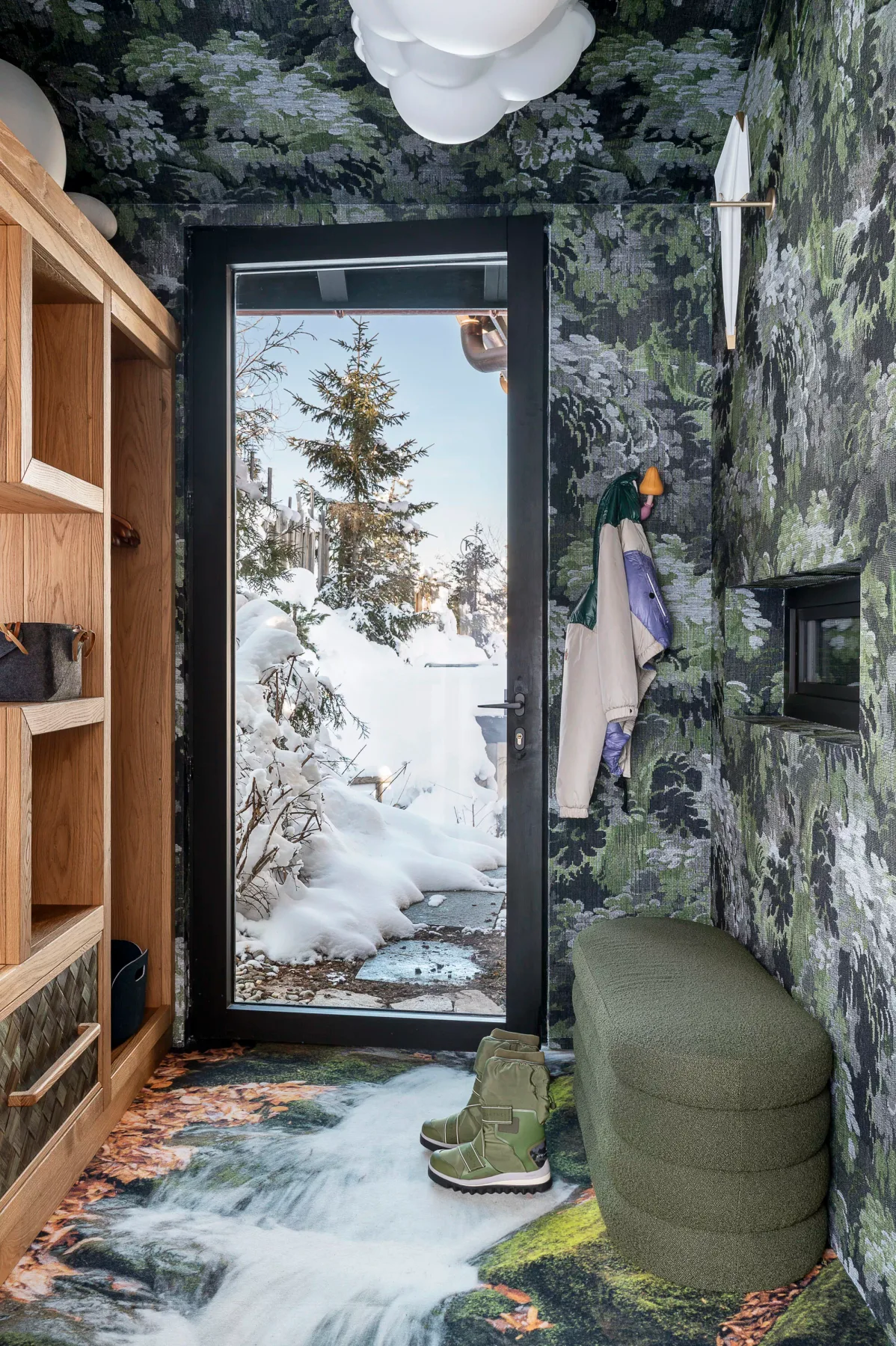 A compact bathroom with patterned walls, a glass door, and a small green seat.