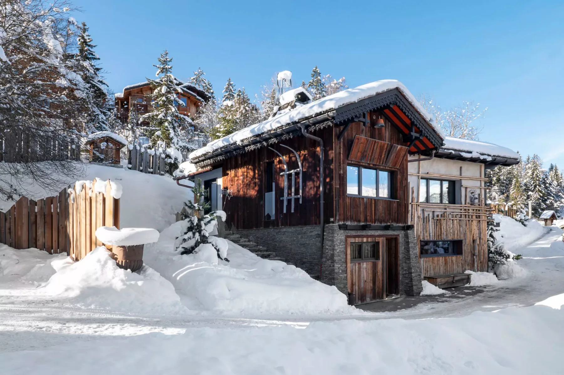 A wooden chalet stands amid deep snow and snow-covered trees.