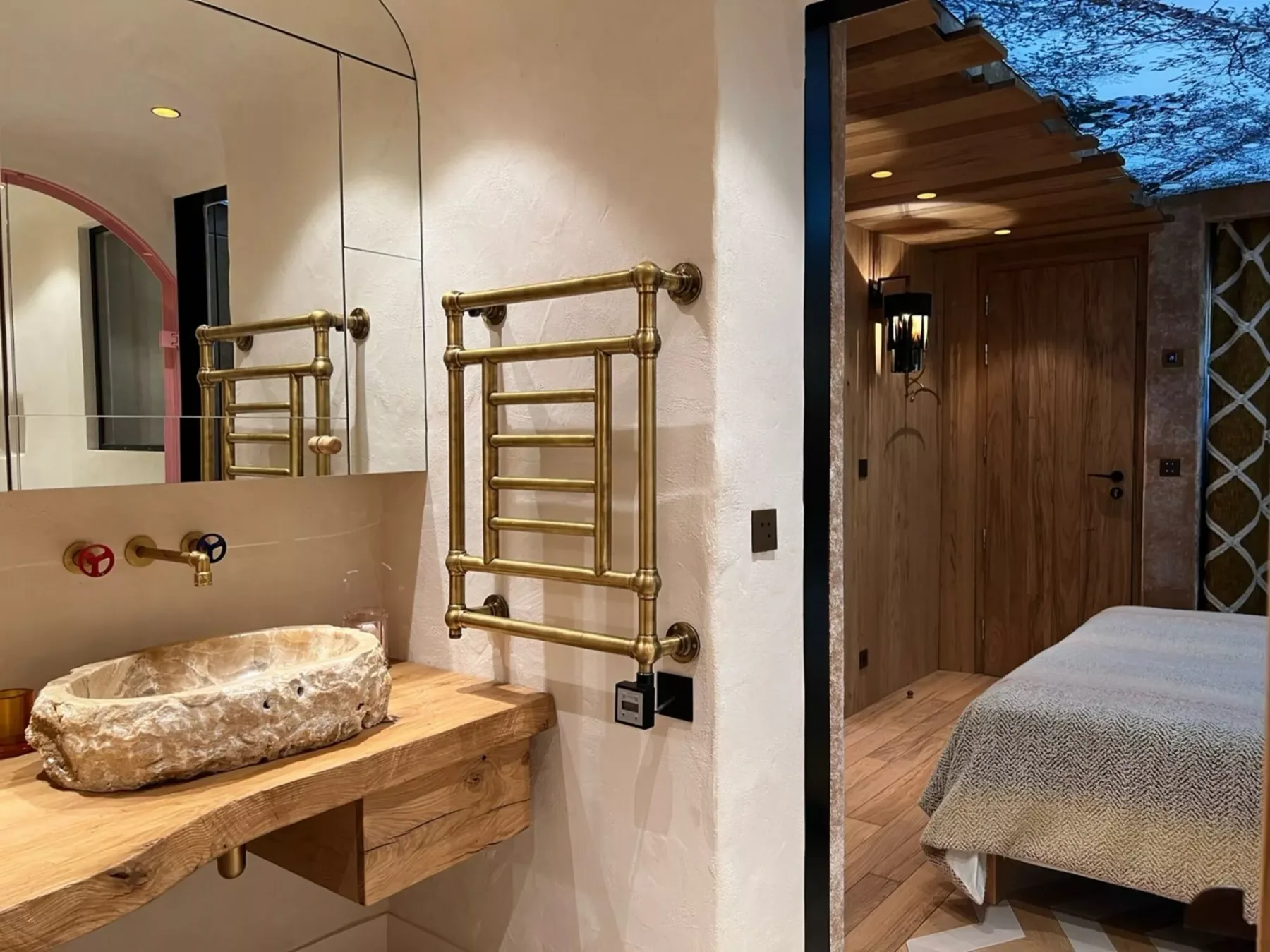A bathroom vanity with a stone basin opens onto a bedroom with a wooden door.