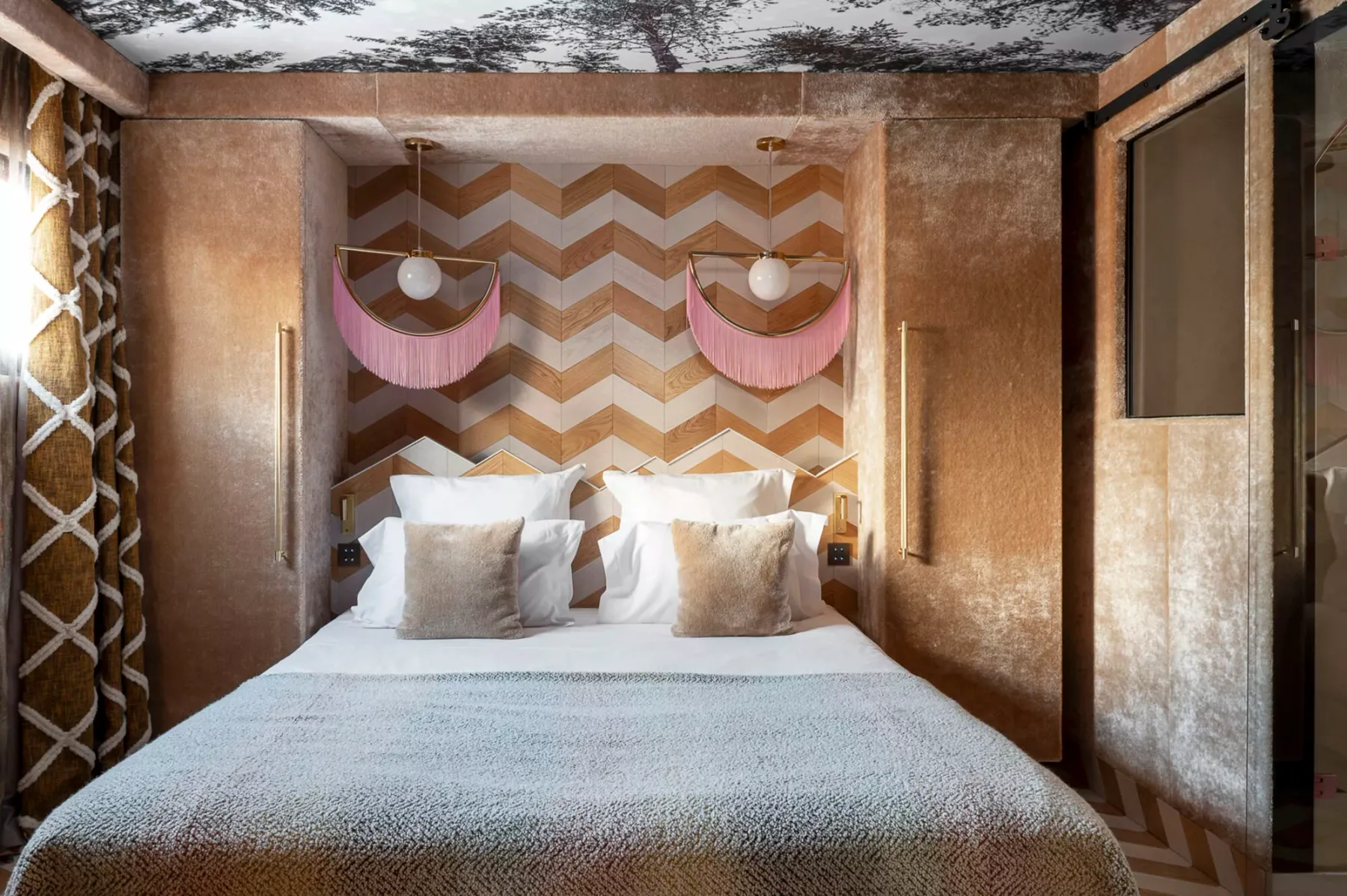 A bedroom with a bed beneath a patterned wall and two decorative lights.