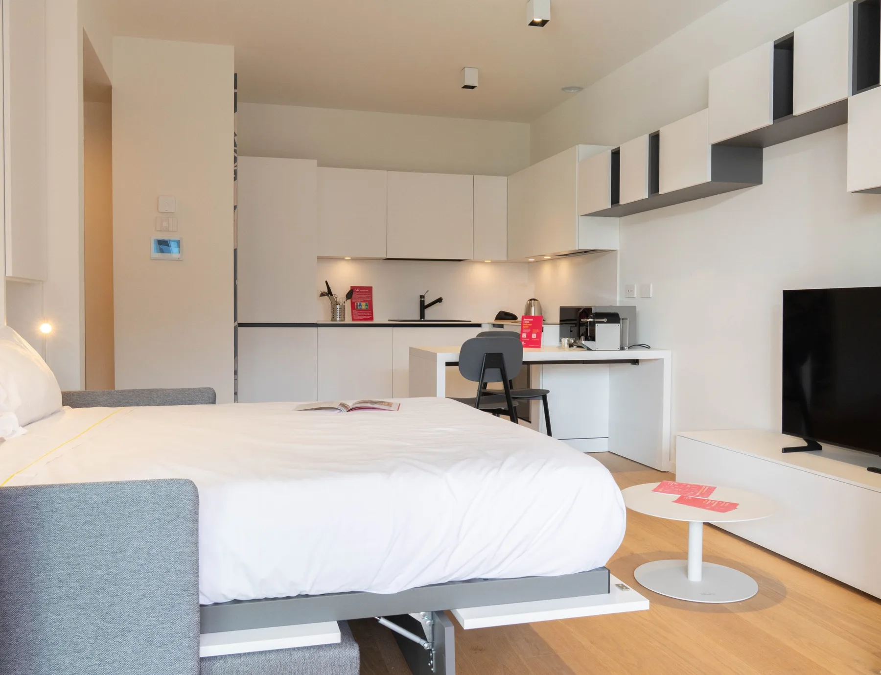 A bedroom and kitchenette share an open space, with a bed in the foreground.