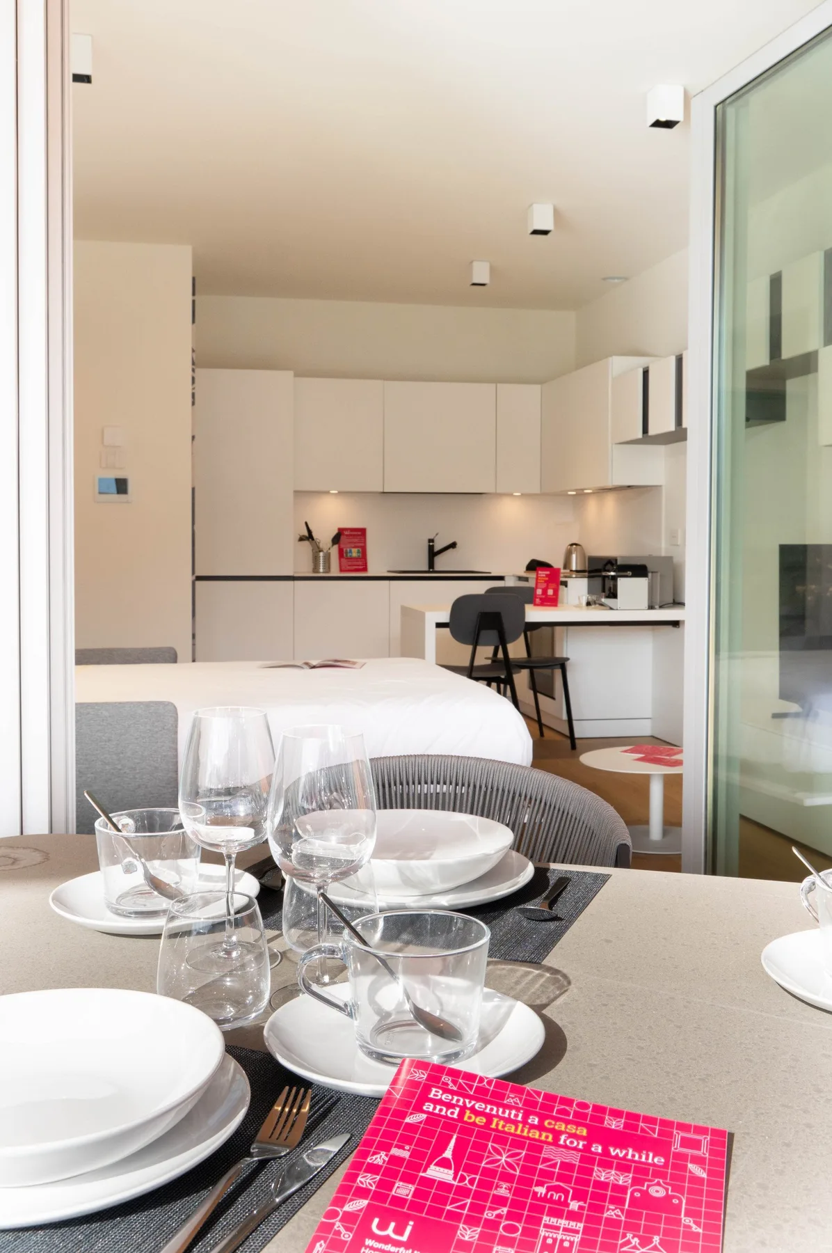 A dining table with place settings sits in front of a bed and kitchenette.