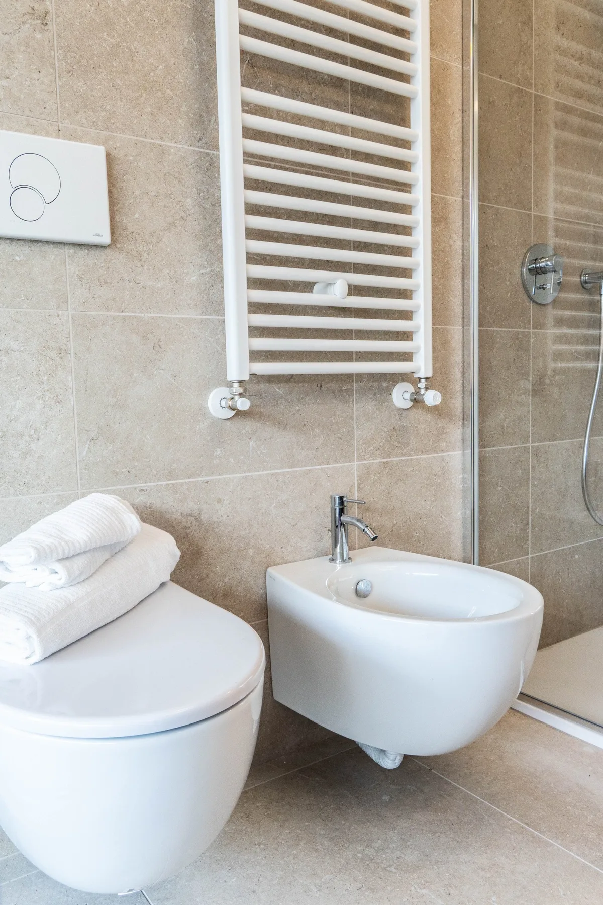 A tiled bathroom with a toilet, wall-mounted bidet, and towel radiator.