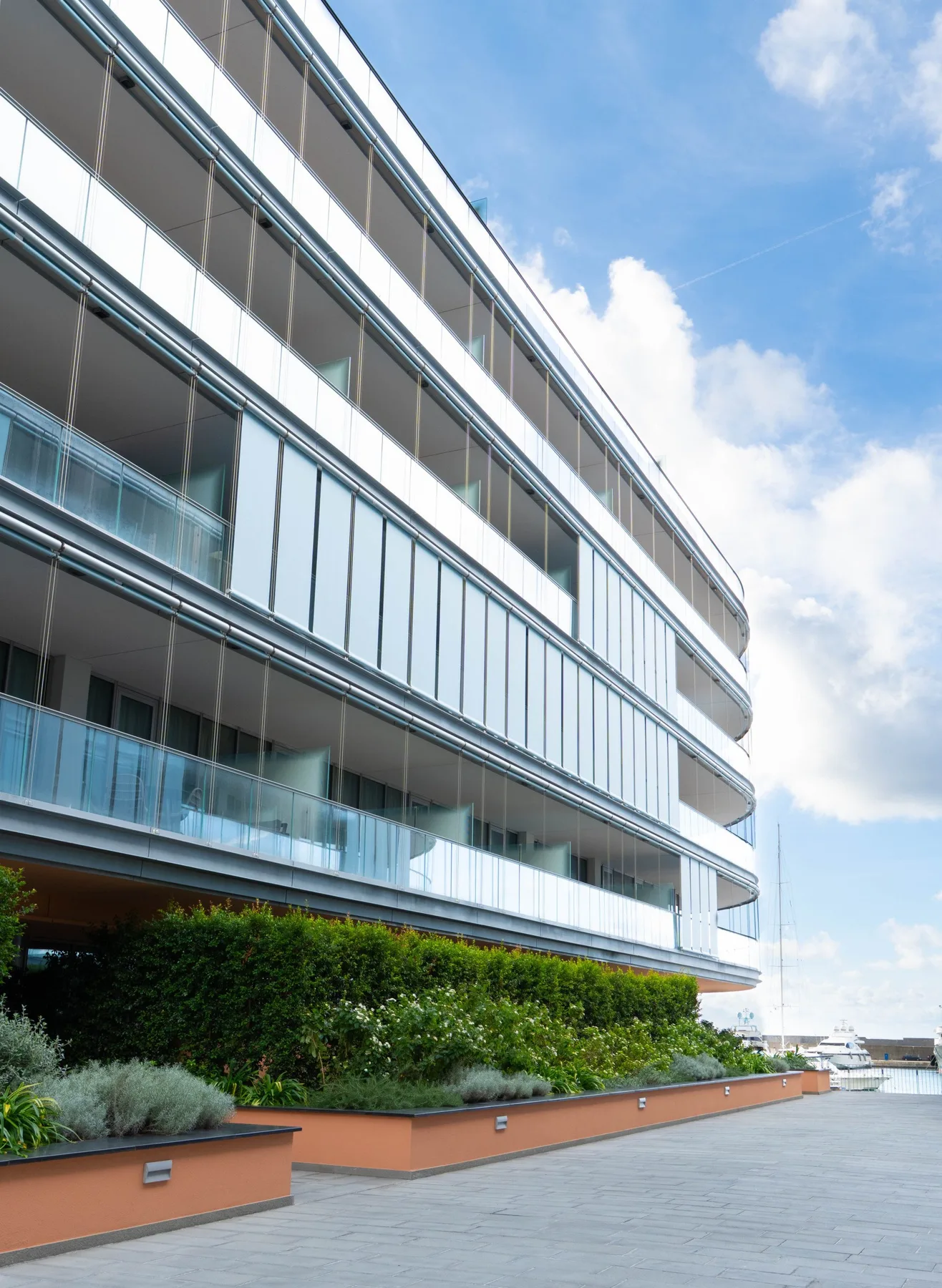 A modern building facade with glass balconies borders a paved outdoor terrace.
