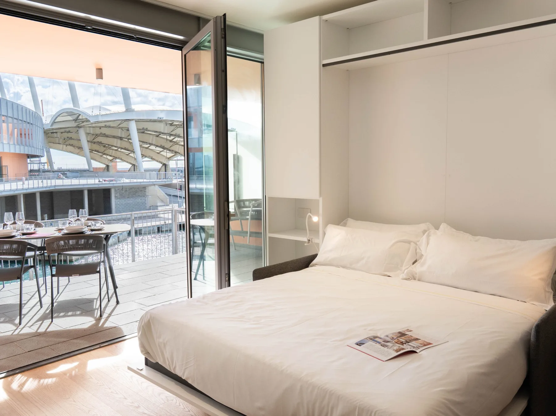 A bedroom with a bed beside an open glass door leading to a terrace.