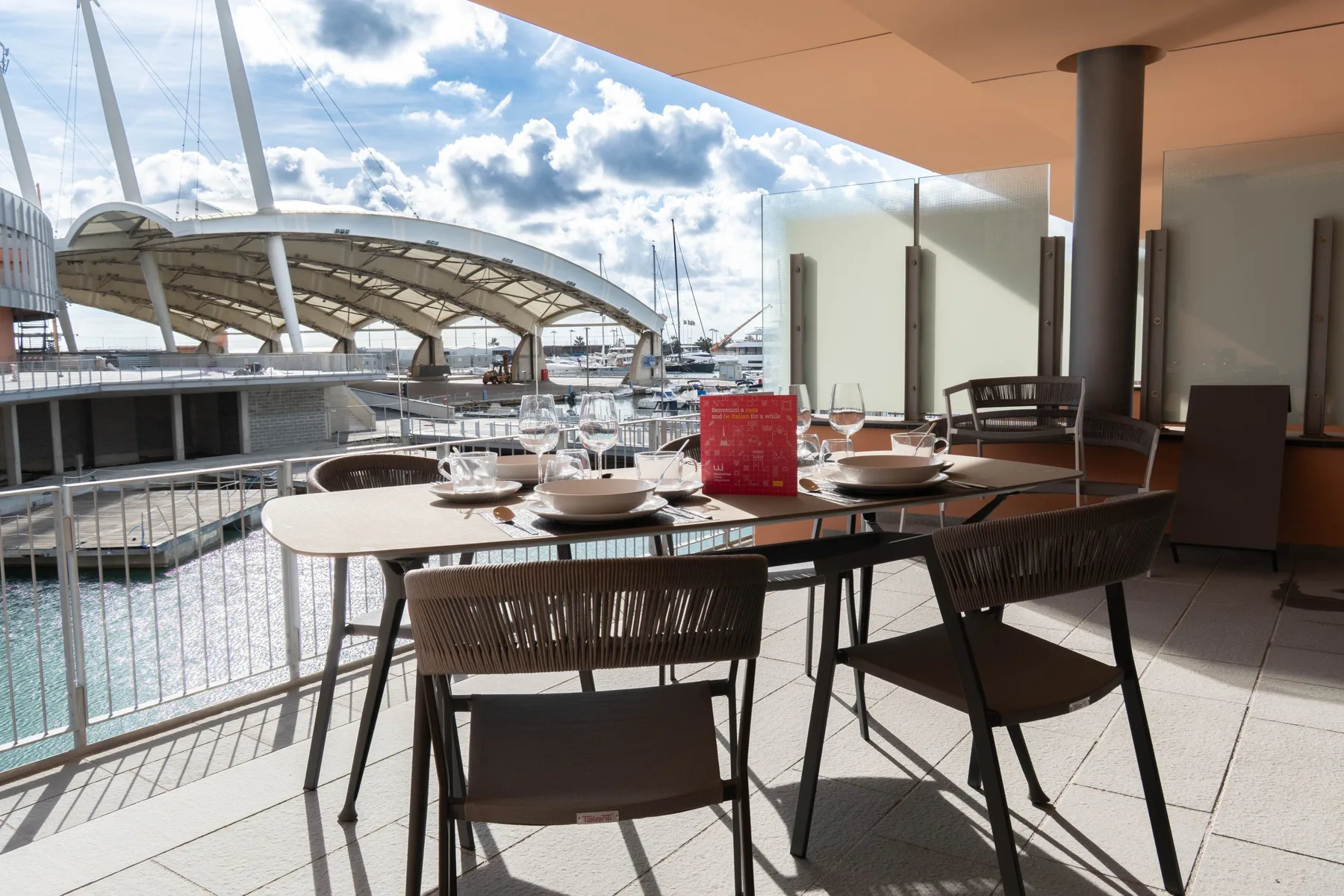 An outdoor dining terrace overlooks a waterfront marina and a large arched bridge.